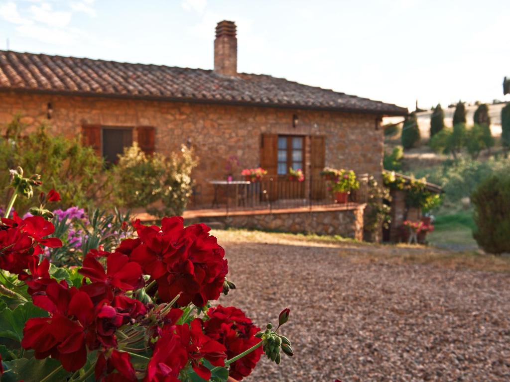 a brick house with red flowers in front of it at Agriturismo La Buca di Bellugi in San Quirico dʼOrcia