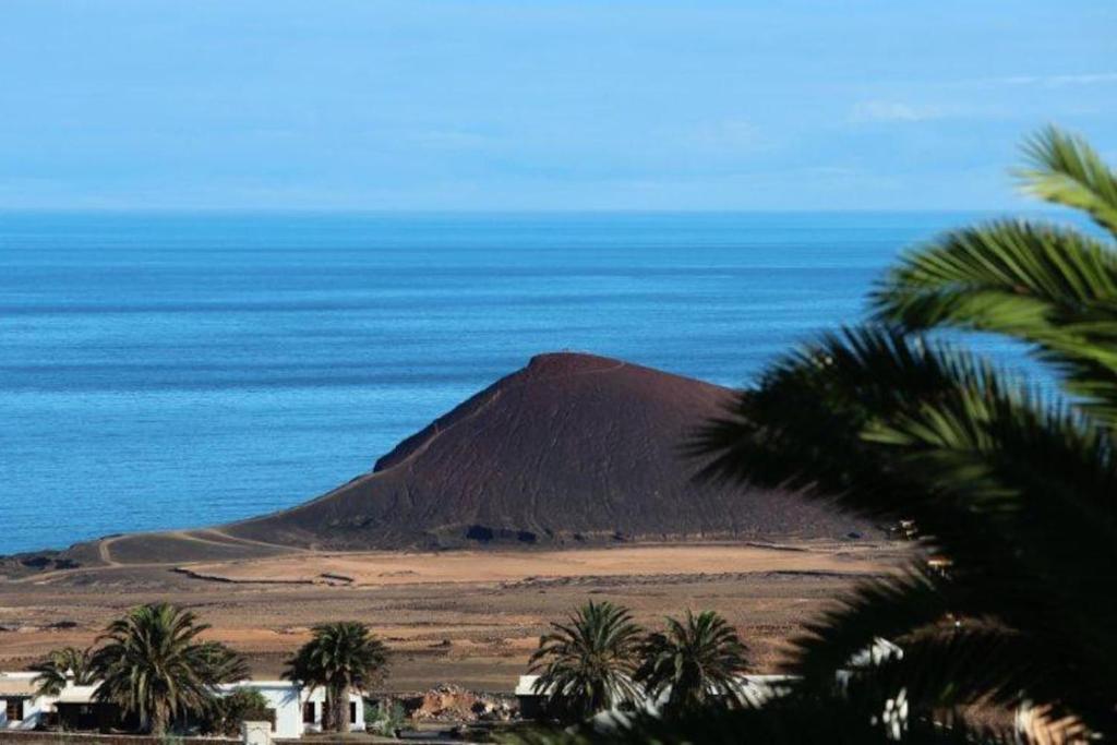 a mountain in the middle of the ocean with palm trees at El Inti 1 in Tinajo