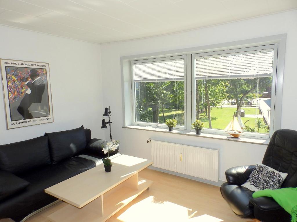 a living room with black leather furniture and windows at Vestergade Holiday Apartment in Frederikshavn