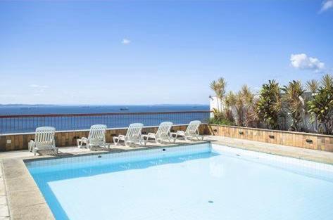 a large swimming pool with chairs and the ocean at Flat Privativo Sol Victoria Marina in Salvador