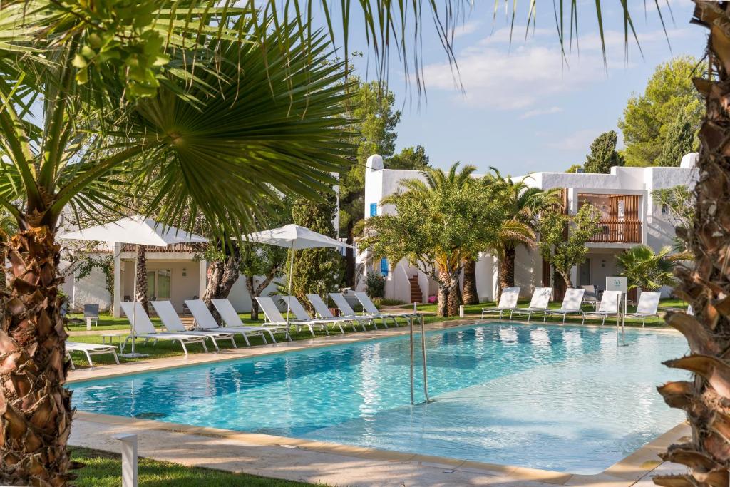 Cala Llenya Resort Ibiza في كالا يينيا: مسبح مع كراسي الصالة والنخيل