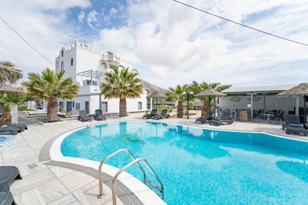 a swimming pool with palm trees and a building at Blackcoast Santorini in Perivolos