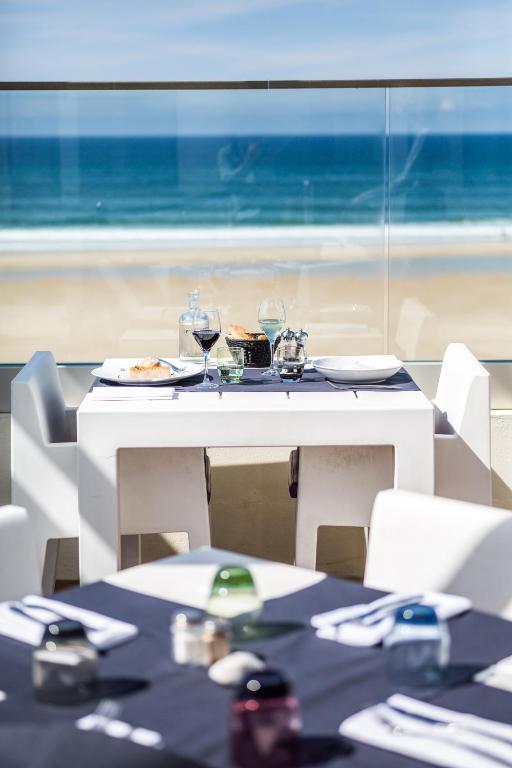 a table with plates of food and wine glasses and the beach at Le Grand Hotel de la Plage in Biscarrosse-Plage