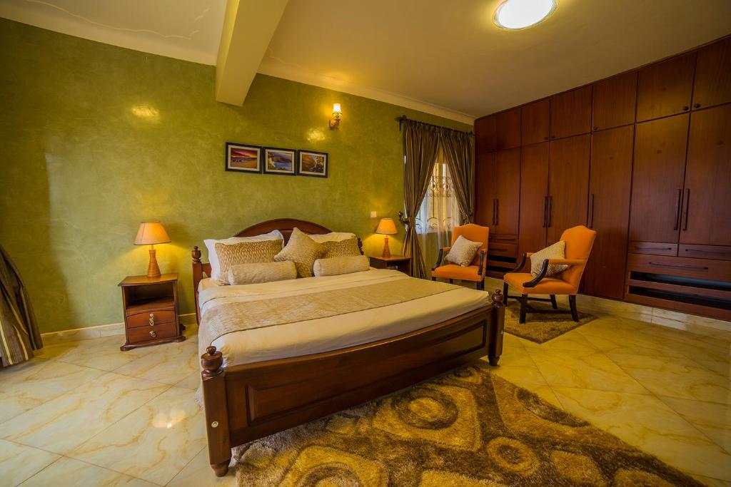 1 Schlafzimmer mit einem großen Bett und 2 Stühlen in der Unterkunft Greens Guest Homes in Mutungo