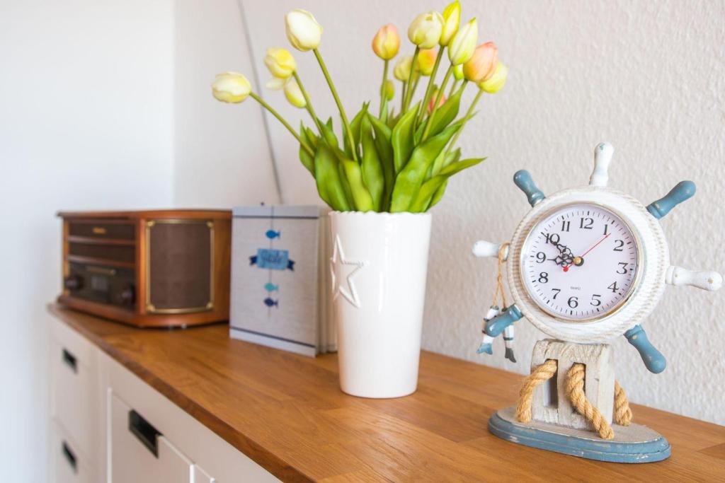 a clock sitting on a table next to a vase of flowers at Haus am Deich Wohnung 4 in Dahme