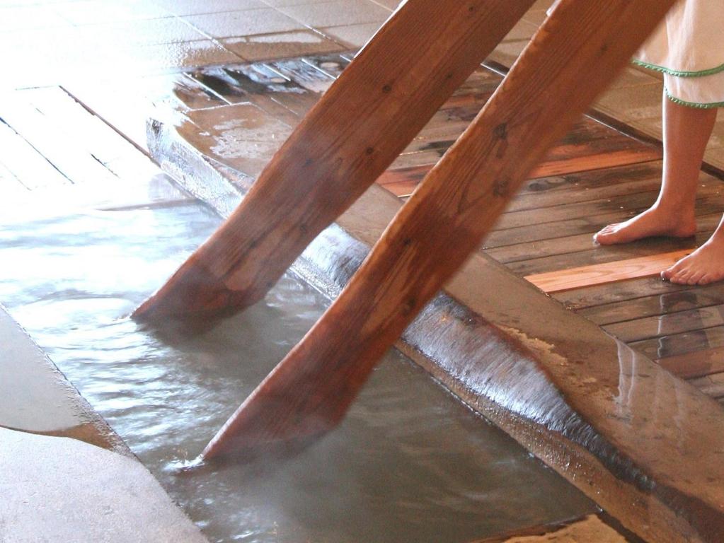 a person standing under a wooden table in water at Kusatsu Onsen Hotel Village in Kusatsu