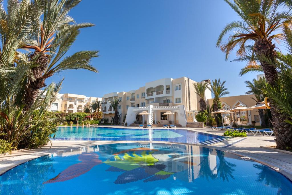 una piscina con palmeras frente a un hotel en Le Corail Appart'Hotel Yasmine Hammamet en Hammamet