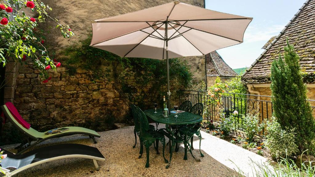 a table and chairs with an umbrella on a patio at Au coeur de Beynac, une maison de caractère avec jardin terrasse in Beynac-et-Cazenac