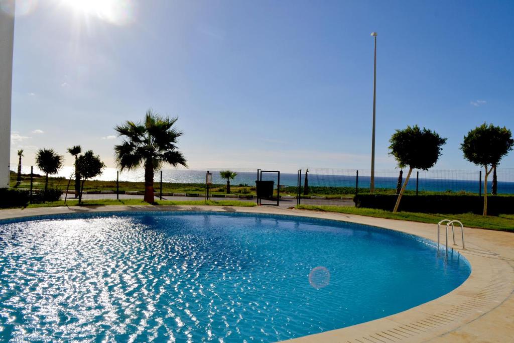 a large blue swimming pool with palm trees and the ocean at Flat Asilah Marina Golf in Asilah
