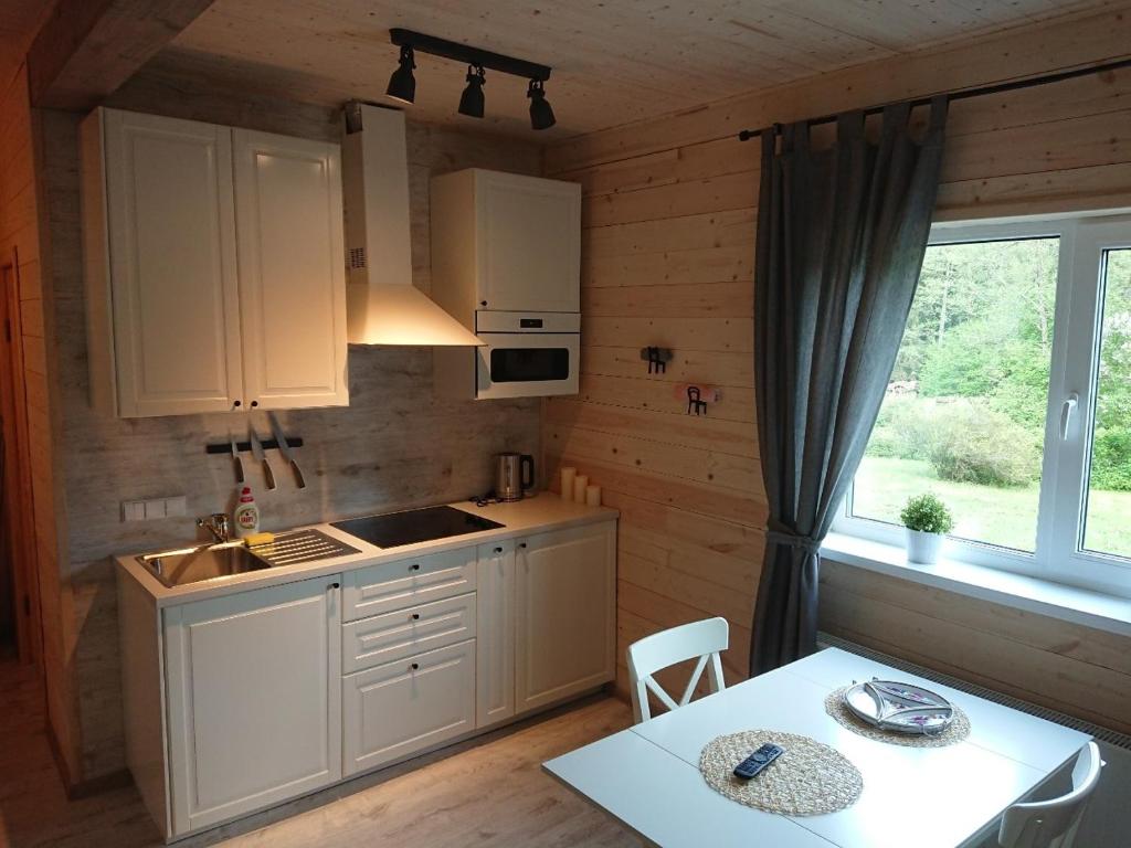 eine Küche mit weißen Schränken, einem Tisch und einem Fenster in der Unterkunft Mizarai Mill House in Druskininkai