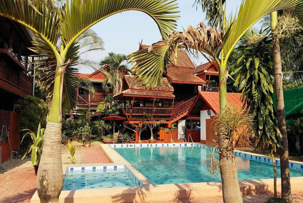 a resort with a swimming pool and palm trees at Golden Teak Home Resort in Saraphi