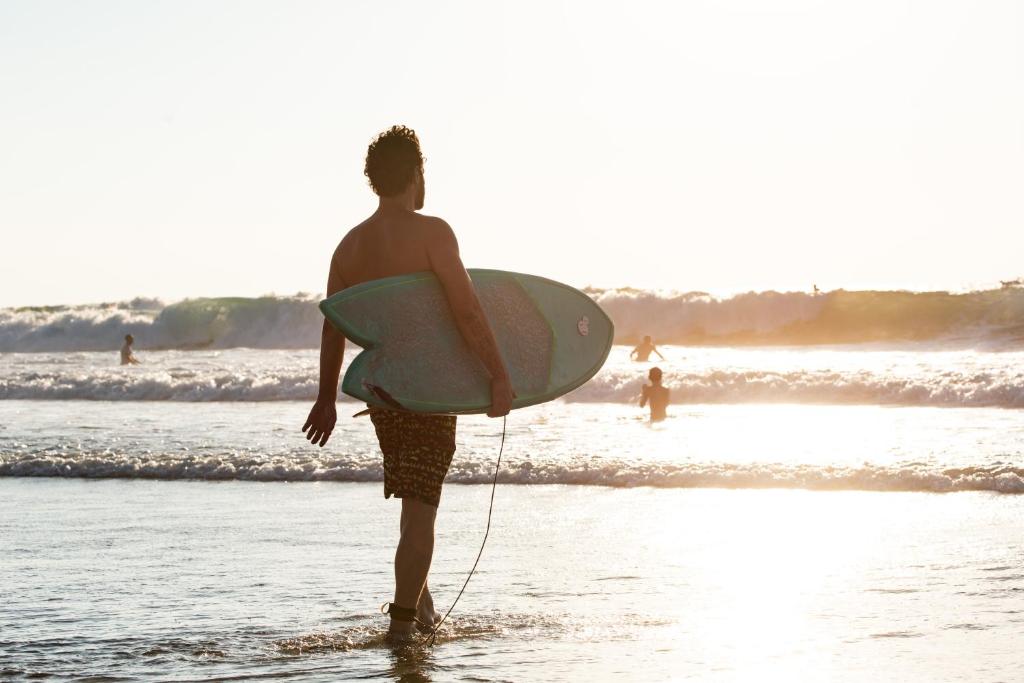 un hombre caminando por la playa con una tabla de surf en The Spot Hostel, en Tel Aviv