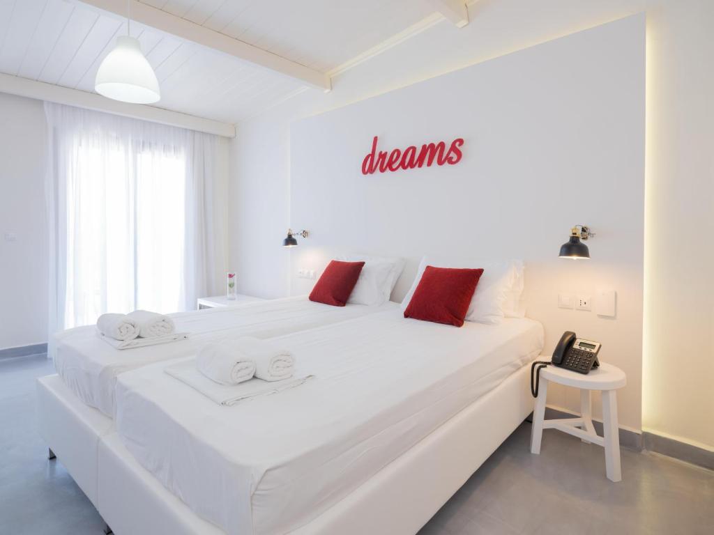 a white bedroom with a large white bed with red pillows at Eva Mare Hotel & Suites - Adults only in Agia Pelagia