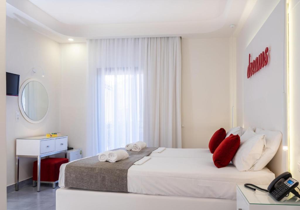 a white bedroom with a large bed with red pillows at Eva Mare Hotel & Suites - Adults only in Agia Pelagia