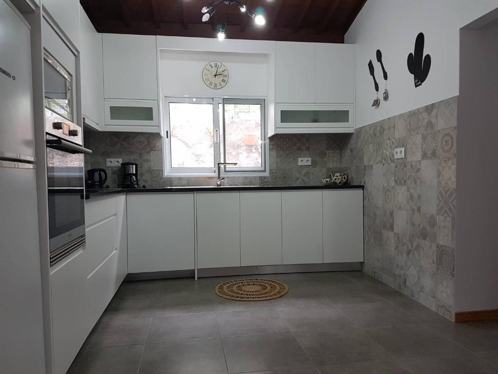 una cocina con armarios blancos y un reloj en la pared en Join our relaxed house near the beach - Mosteiros en Mosteiros