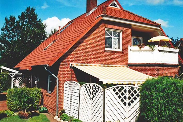 a red brick house with a white fence in front of it at Ferienwohnung Nowara in Krummhörn