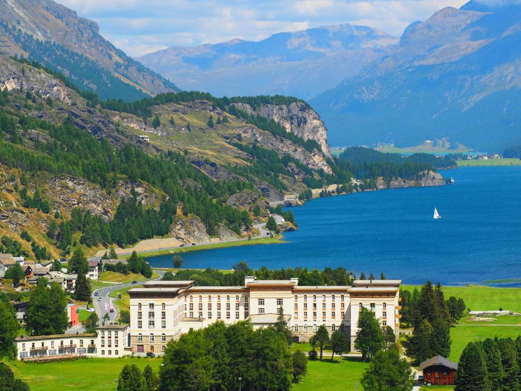 Maloja Palace Residence Engadin-St Moritz CO2-Neutral في مالويه: مبنى كبير على تلة بجوار تجمع للمياه