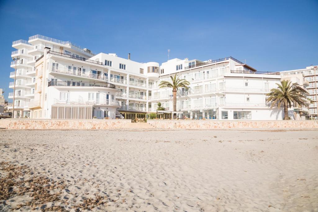 a large white building with palm trees in front of a beach at Hotel Club S'Illot in S'Illot