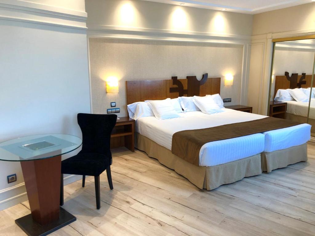 バリャドリッドにあるHotel Olidの大きなベッドとテーブルが備わるホテルルームです。