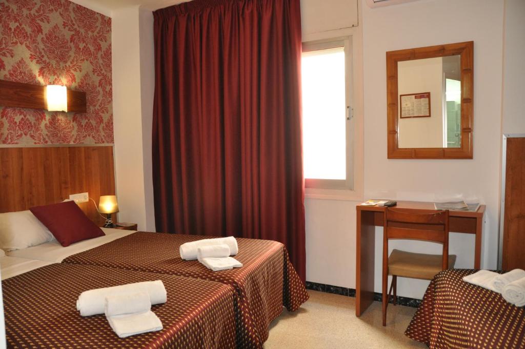 Habitación de hotel con 2 camas, escritorio y espejo. en Hostal - Pensión El Amigo, en Lloret de Mar