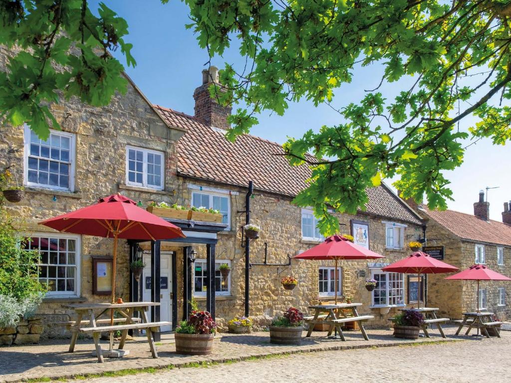 an inn with picnic tables and umbrellas in front of it at The Fauconberg in Coxwold