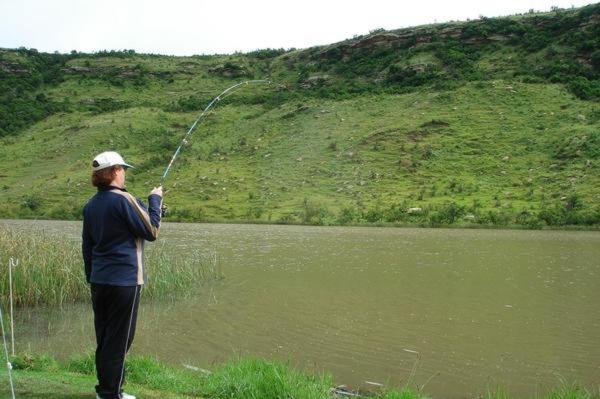 una mujer parada junto a un lago sosteniendo una caña de pescar en MacFarlanes, en Harrismith