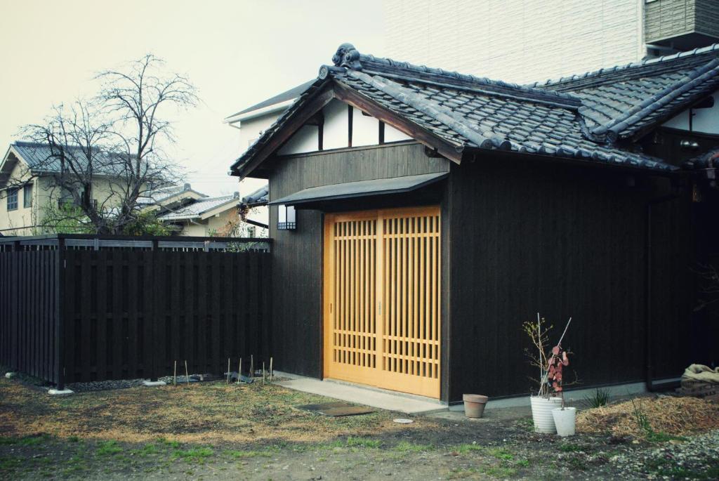 a black house with a wooden door next to a fence at NARAigoto EENA HOUSE in Nara
