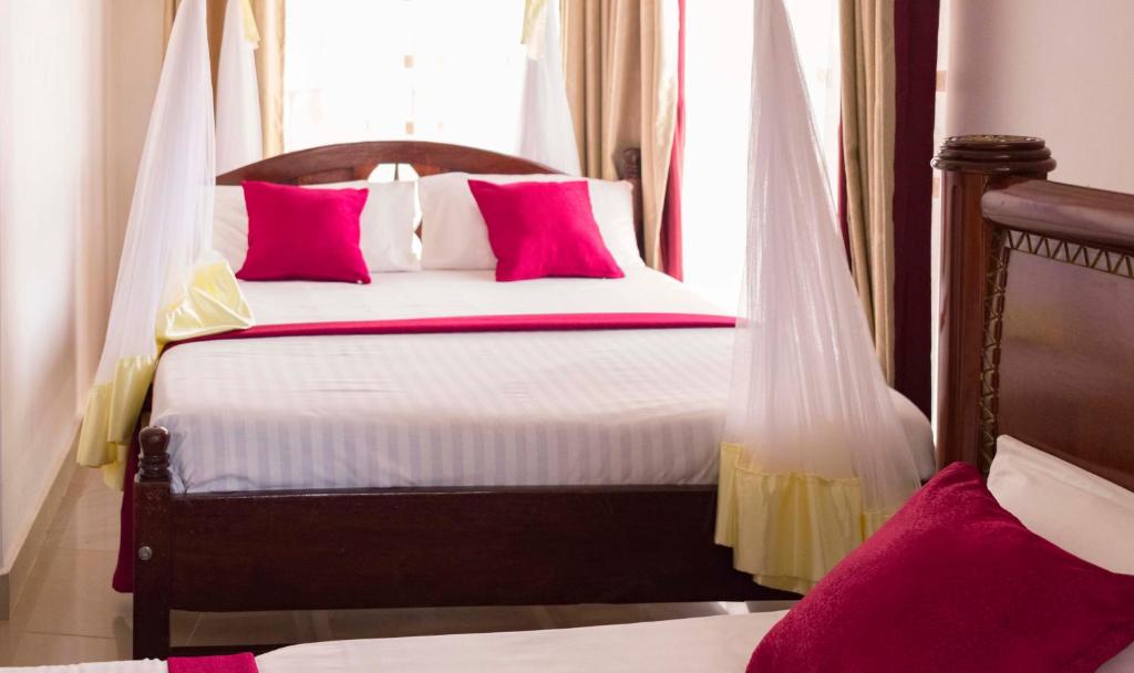 a bedroom with a bed with pink pillows and a window at Sienna Beach Hotel Entebbe in Entebbe