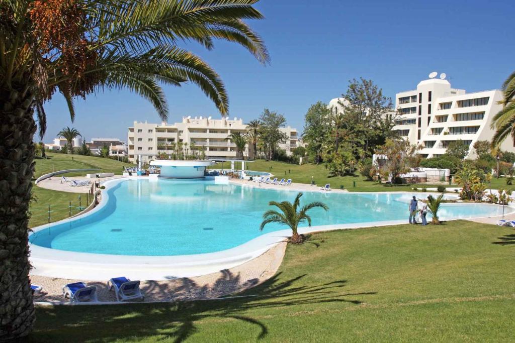 une grande piscine avec des palmiers et des bâtiments dans l'établissement Alvor Retreat at Vila Marachique, à Alvor