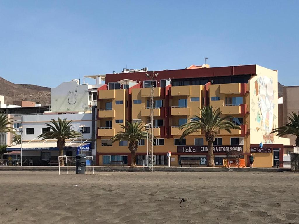 a building on the beach with palm trees in front at El rincon de Maruca in Gran Tarajal