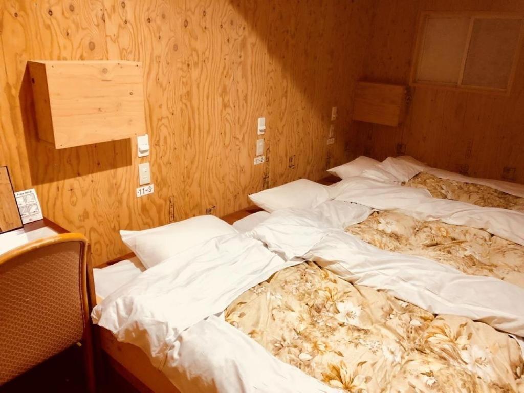 two unmade beds in a room with wooden walls at Guesthouse Otaru Wanokaze triple room / Vacation STAY 32203 in Otaru