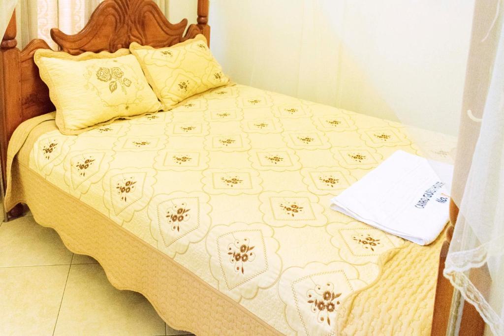a bed with a yellow and white quilt on it at Japs Motel Mbarara in Ruhendwa