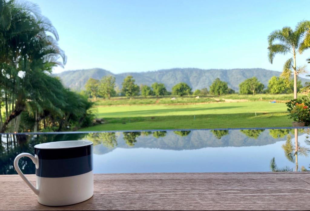 una tazza di caffè seduta su un tavolo di fronte a un campo da golf di Annie Villa at Khao Yai a Mu Si