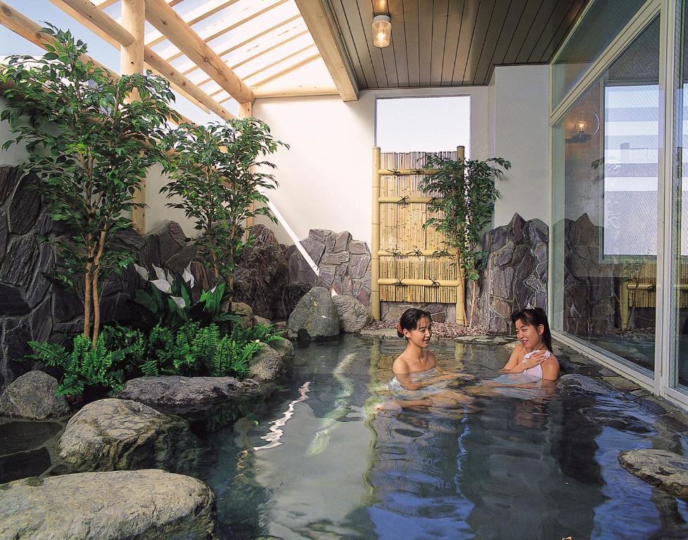 two women sitting in a hot tub in a garden at Hotel Yuzawa Yuzawa Denkiya in Yuzawa