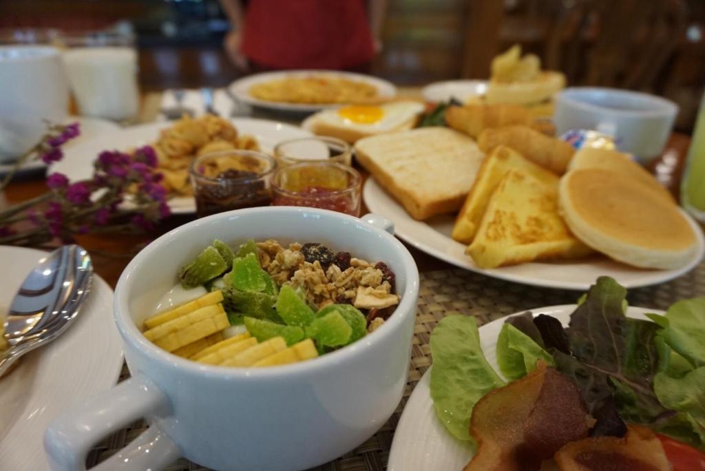 A breakfast spread with fruit, cereal, salad, bread, pancakes and cooked dishes.