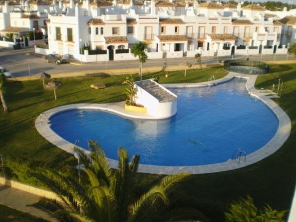 een groot blauw zwembad met gebouwen op de achtergrond bij Apart Club la Barrosa in Chiclana de la Frontera