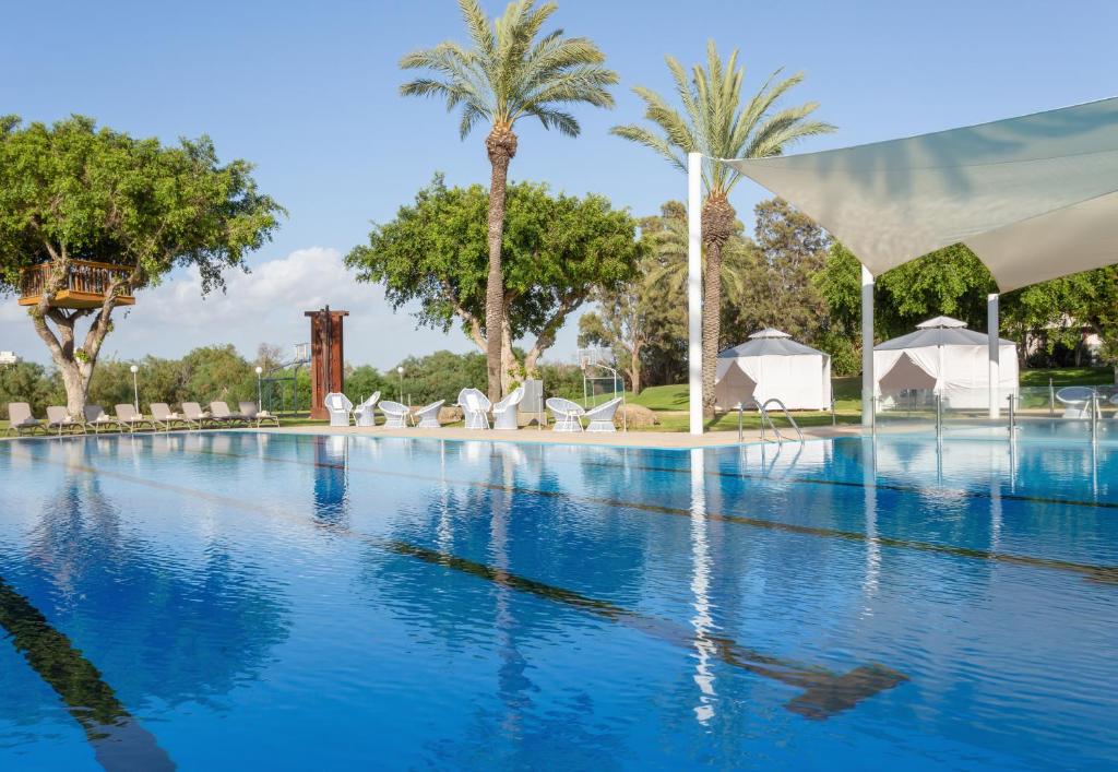 una gran piscina con palmeras y tiendas blancas en Dan Caesarea Resort en Caesarea