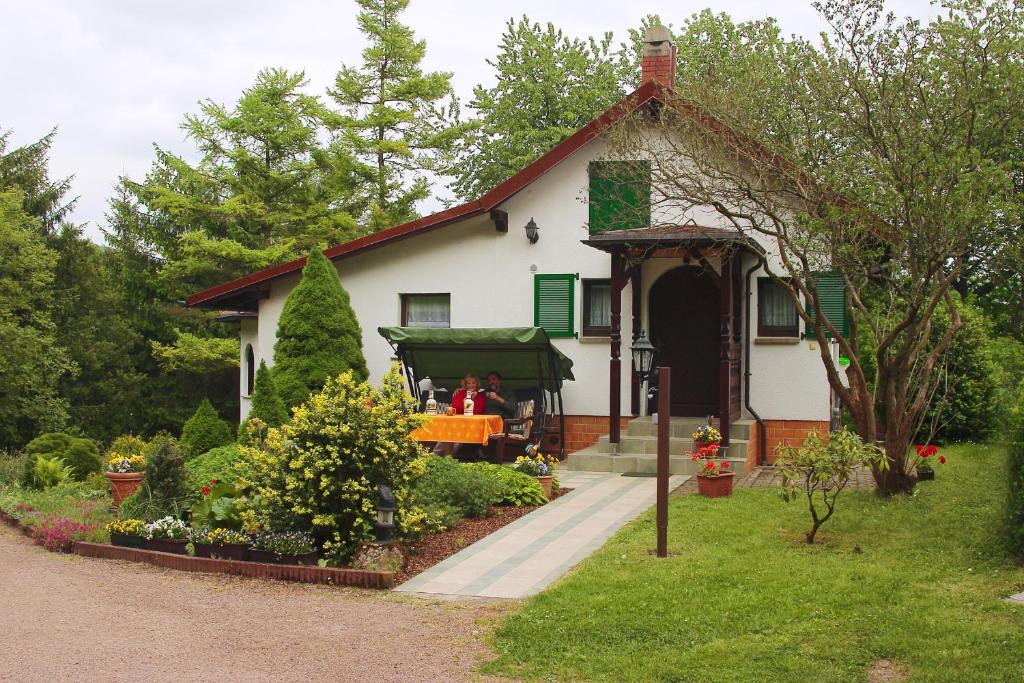 une petite maison avec des personnes assises sur la terrasse couverte dans l'établissement Haus Christina, à Bad Liebenstein