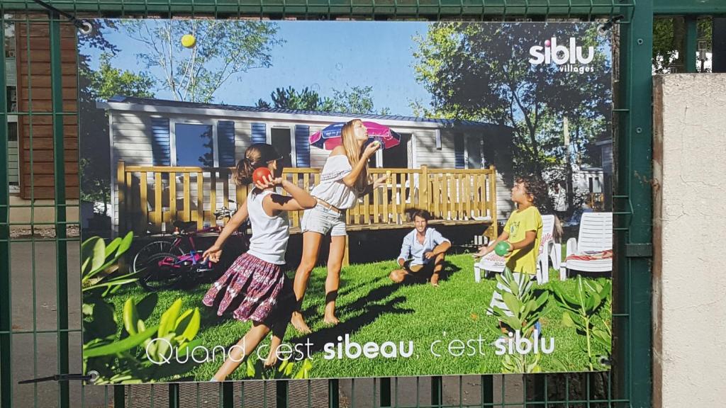 un cartel en una valla con tres chicas jugando béisbol en Particulier loue mobil-home dans le parc siblu, en Saint-Brevin-les-Pins