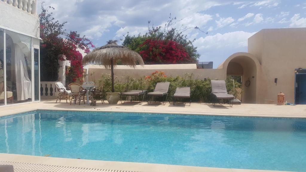 a swimming pool with chairs and a table and an umbrella at Menzel Churasco Djerba in Aghīr