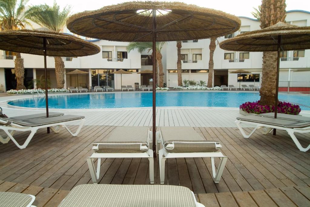 2 Stühle und Sonnenschirme neben einem Pool in der Unterkunft Leonardo Privilege Eilat Hotel - All inclusive in Eilat