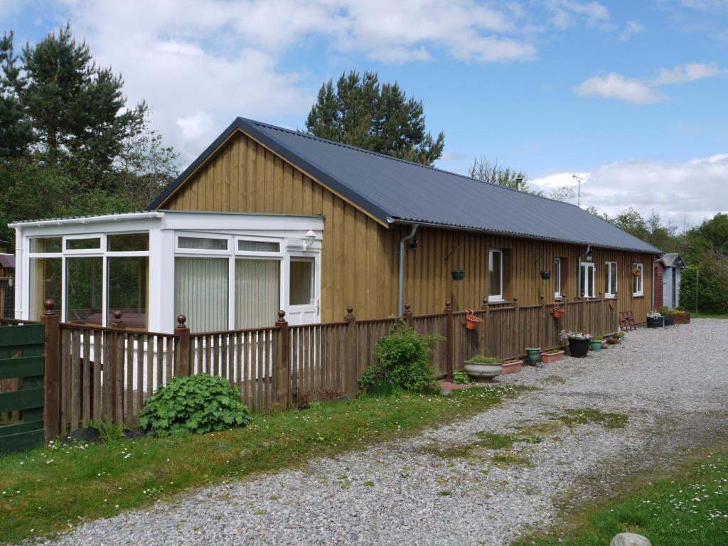 a wooden building with a fence and a house at Roe Deer Cottage in Beauly