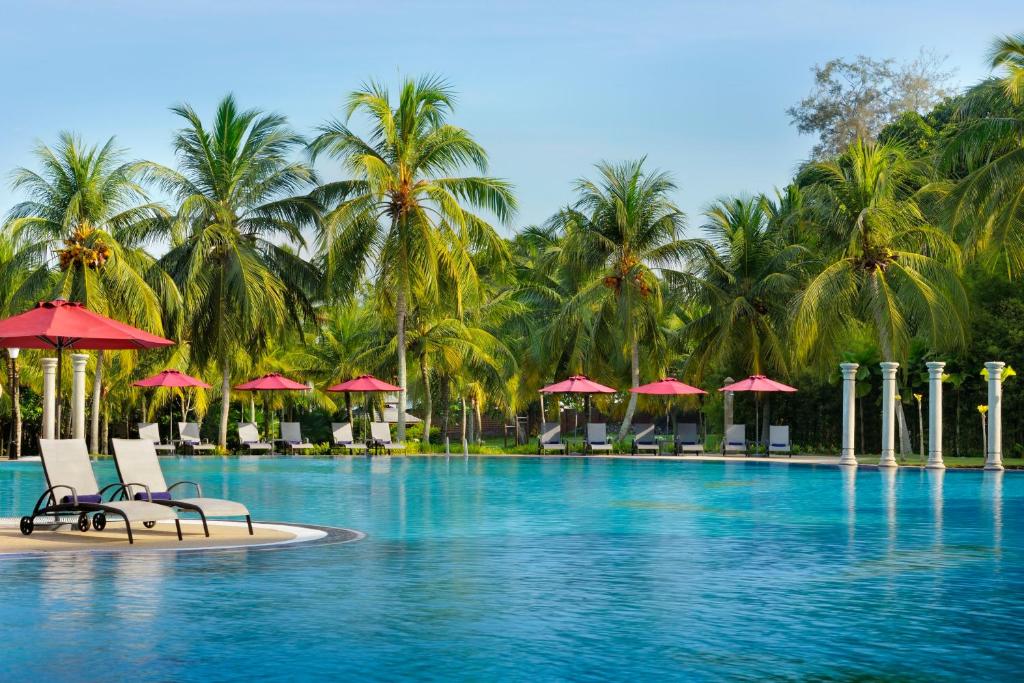 una piscina con palme, sedie e ombrelloni di Thistle Port Dickson Resort a Port Dickson