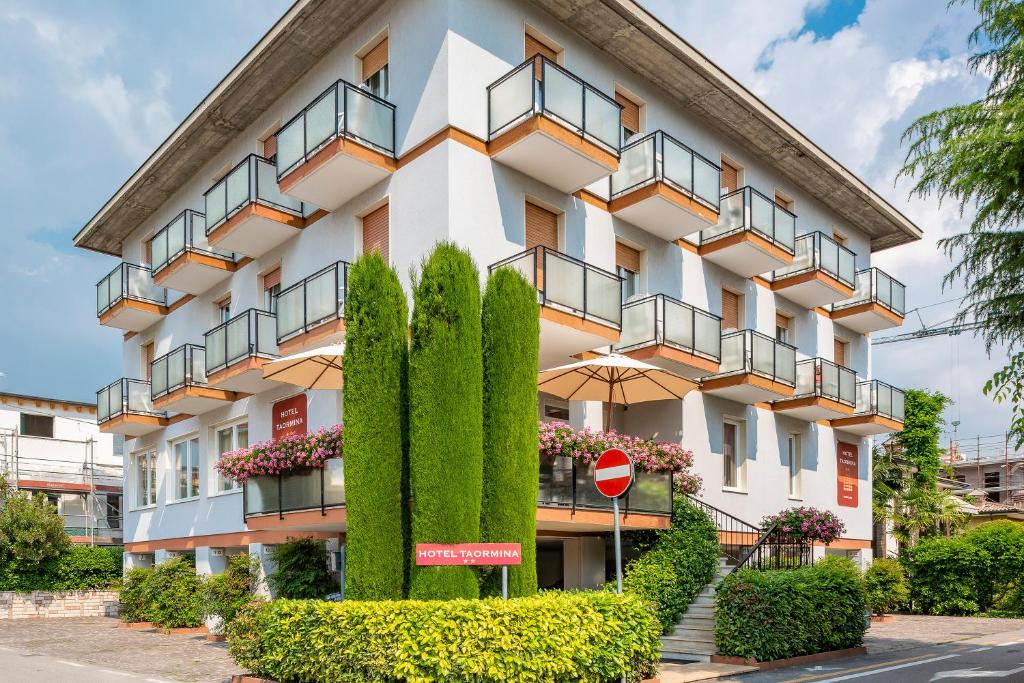 un immeuble d'appartements avec des buissons devant lui dans l'établissement Hotel Taormina, à Bardolino