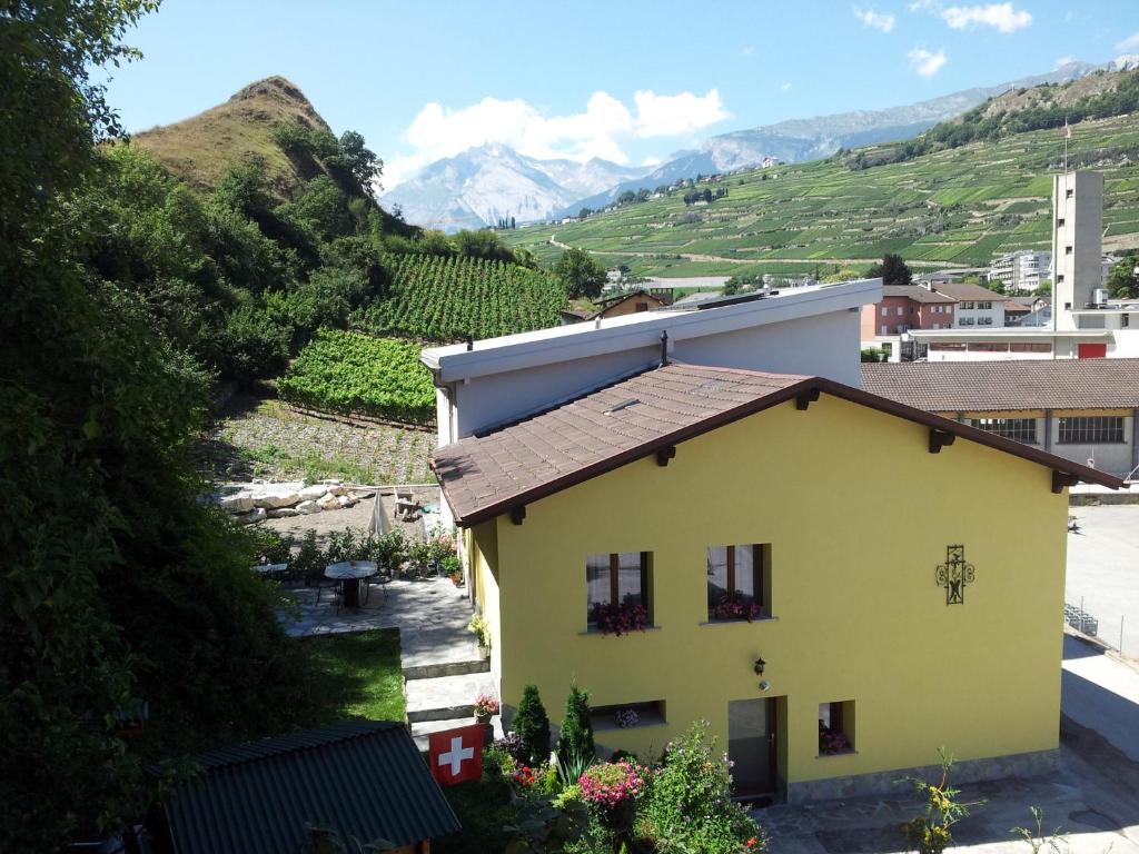 une maison jaune avec des montagnes en arrière-plan dans l'établissement Le Merle Châtelain, à Sion