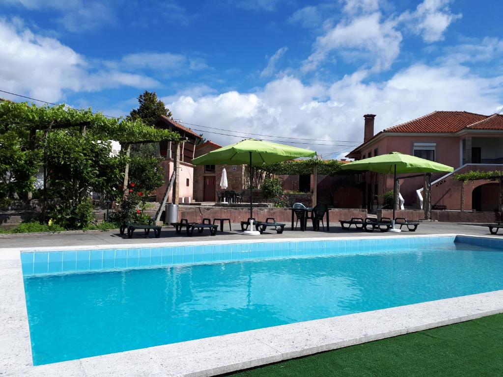 uma piscina com guarda-sóis verdes e uma casa em Quintinha de Santiago em Oliveira de Azemeis
