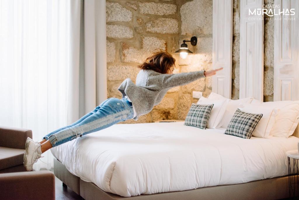 a woman is jumping on a bed at Casa das Muralhas in Covilhã