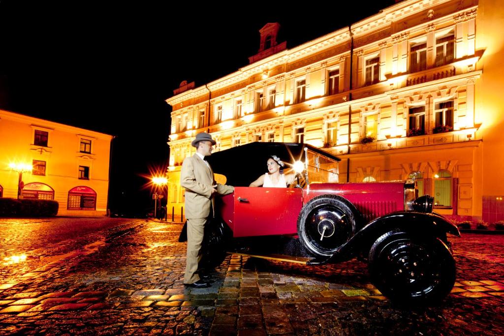 a man and a woman standing next to a red car at Hotel Havel in Rychnov nad Kněžnou