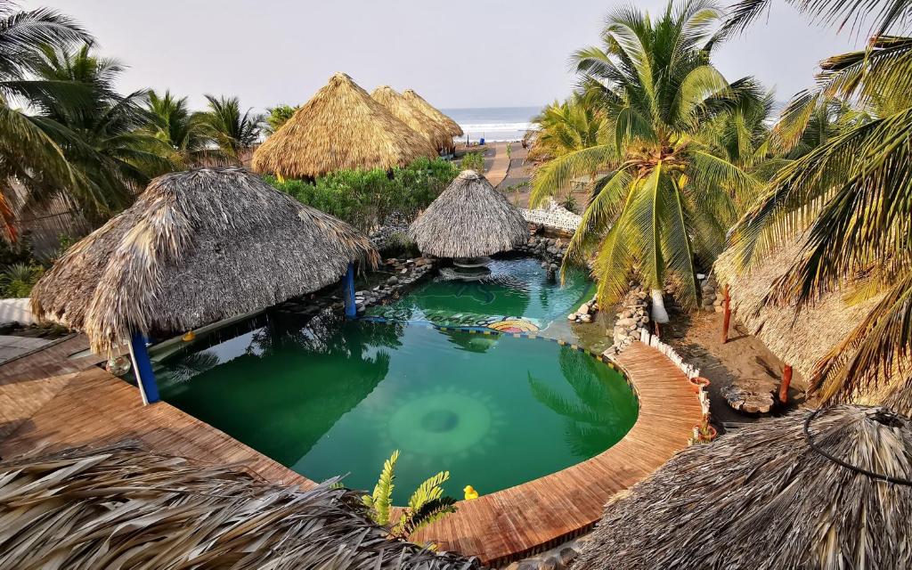 a swimming pool with thatched huts and palm trees at Eco-Hotel Playa Quilombo in Las Lisas