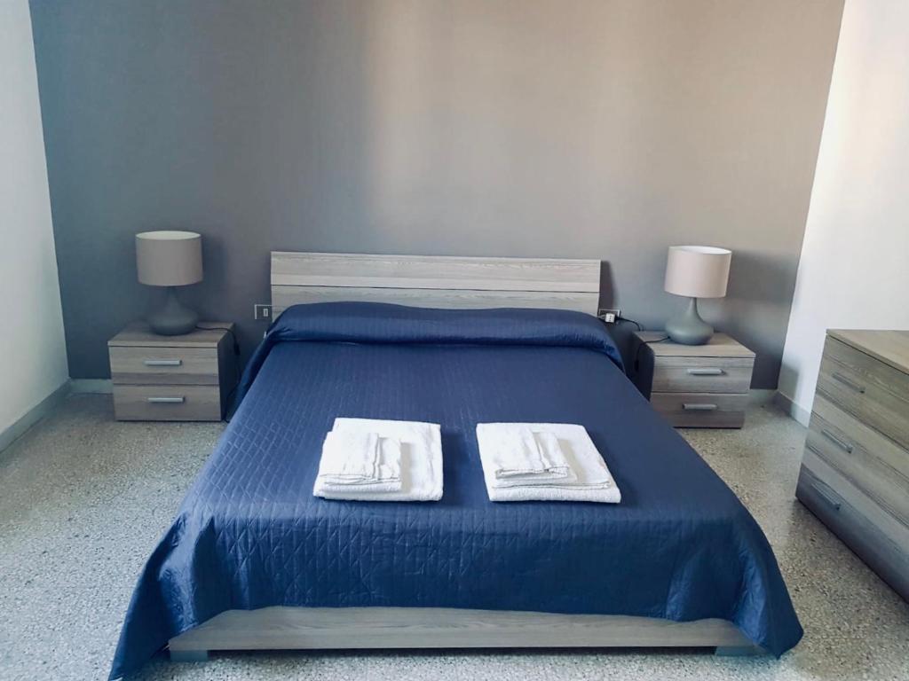 マティーノにあるAppartamento Via del Mareのベッドルーム1室(青いベッド1台、テーブル2台、タオル2枚付)